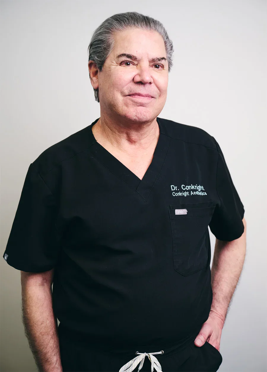 J. Michael Conkright, MD in black medical scrubs standing against white background for professional portrait - Doctor in Evansville, IN