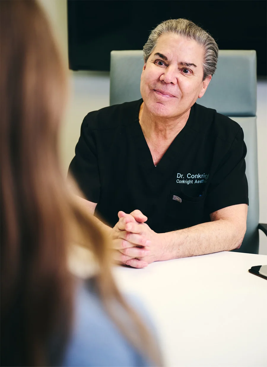 Doctor James Michael Conkright MD in black scrubs consulting with patient across desk in clinical setting - in Evansville, IN